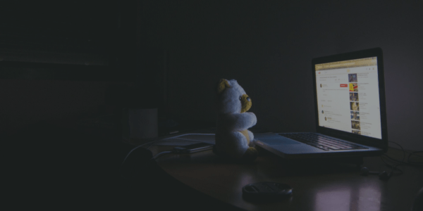 A teddy bear is looking at a laptop monitor